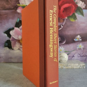 May include: A red hardcover book with gold lettering on the spine. The title is "The Complete Short Stories of Ernest Hemingway". The book is published by Scribner's.