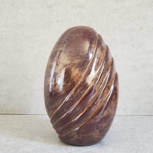May include: A brown ceramic vase with a swirling, textured design. The vase has a glossy finish and a light brown glaze.