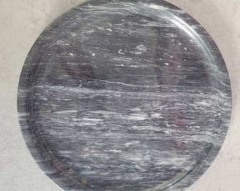 May include: A round, gray marble tray with a white swirl pattern. The tray is perfect for serving snacks or displaying decorative items.