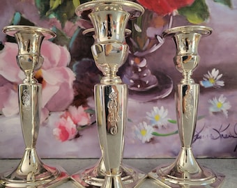 May include: Three silver candle holders with a hexagonal base and ornate detailing. The candle holders are arranged in a row on a table.