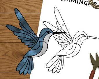 May include: A wooden surface displays a hummingbird stained glass pattern, alongside tools including pliers, tape, and a tape measure. The pattern is a line drawing with numbered sections. White spectacles and a glass cutter are also present.