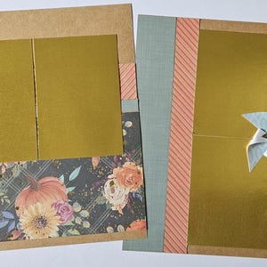 May include: Two scrapbook pages with gold panels and decorative paper. One page features a pinwheel and a label that reads "gather with grateful hearts." The other page has a pinwheel. Floral and pumpkin patterns are visible.