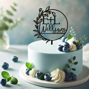 May include: Black acrylic cake topper with a floral wreath and a circle containing the initials "E+L" and the text "William 05.22.25".
