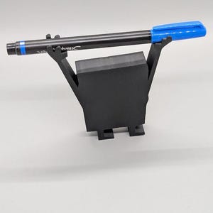 Puede incluir: Un portal&aacute;pices negro con un bol&iacute;grafo negro y una tapa azul. El bol&iacute;grafo descansa sobre un soporte negro de forma geom&eacute;trica. El bol&iacute;grafo tiene la palabra "Sharpie" impresa.