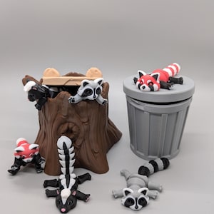 May include: A collection of miniature animal figurines, including raccoons, a skunk, and a red panda. The figurines are in various poses, some near a tree stump and a gray trash can. The animals are painted in their natural colors.