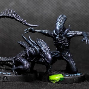 May include: Four black Alien figures in various poses, each on a round base with a green accent. The figures have detailed skeletal structures and elongated heads, with their tails curved or extended. The figures are painted in a dark, glossy finish.