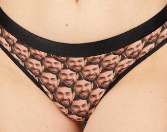 Op de afbeelding: Een onderbroek met een herhaald patroon van lachende gezichten. De onderbroek heeft een zwarte tailleband en afwerking. De achtergrond is een vage interieurscène.