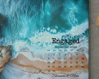 Könnte beinhalten: Ein Schneidebrett mit einem Foto einer Strandszene mit türkisfarbenem Wasser und einer felsigen Klippe. Der Text "Engaged" ist oben auf dem Brett gedruckt, gefolgt von einem Kalender für September 2024. Die Namen "Shannon & Mike" sind unten auf dem Brett gedruckt.