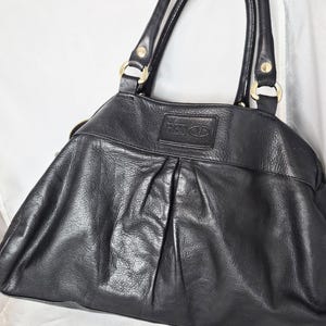 May include: Black leather handbag with gold-coloured hardware. The bag has a pleated design on the front and a top zip closure. The brand name "RED VALENTINO" is embossed on a leather patch.