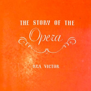 Op de afbeelding: Een rode en witte boekomslag met de titel "The Story of the Opera" en de tekst "RCA Victor" en "Radio Corporation of America". De omslag heeft een decoratief ontwerp met een gestileerde afbeelding van een operazanger.