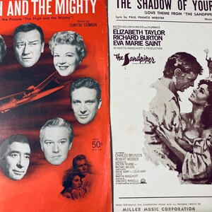 Puede incluir: Dos portadas de partituras musicales vintage. La portada de la izquierda es roja y presenta una foto de un avión y actores de la película "The High and the Mighty". La portada de la derecha es blanca y presenta una foto de Elizabeth Taylor y Richard Burton de la película "The Sandpiper".