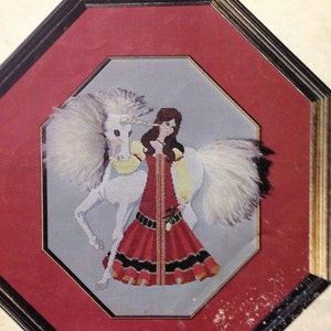 May include: A cross-stitch pattern featuring a white unicorn with a silver horn and a woman in a red and black dress. The title of the pattern is "The Elusive Unicorn".