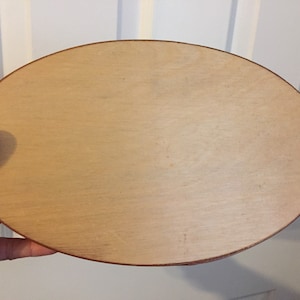 Könnte beinhalten: Eine ovale Holzschale mit hellbrauner Oberfläche und dunklerem braunen Rand. Die Schale wird von einer Hand gehalten. Der Hintergrund ist eine weiße Tür.
