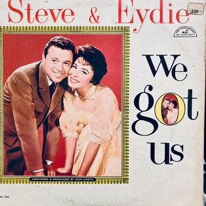 Könnte beinhalten: Vintage Vinyl-Schallplattenhülle mit Steve & Eydie. Das Cover hat einen roten Hintergrund mit einem Foto des Paares. Der Albumtitel "We Got Us" steht in großen schwarzen Buchstaben. Das Cover enthält auch den Text "Arranged & Produced by Don Costa."