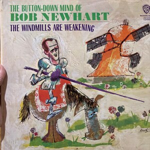 Może przedstawiać: Okładka winylowego albumu z epoki z ilustracją kresk&oacute;wkową mężczyzny jeżdżącego konno z wiatrakiem w tle. Album nosi tytuł "The Button-Down Mind of Bob Newhart: The Windmills Are Weakening".
