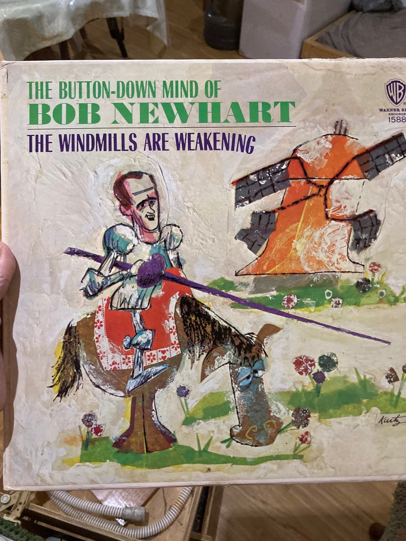 Może przedstawiać: Okładka winylowego albumu z epoki z ilustracją kresk&oacute;wkową mężczyzny jeżdżącego konno z wiatrakiem w tle. Album nosi tytuł "The Button-Down Mind of Bob Newhart: The Windmills Are Weakening".