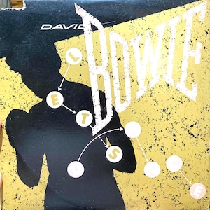 Könnte beinhalten: Albumcover mit dem Namen "DAVID" oben und "BOWIE" in großen weißen Buchstaben. Auf der linken Seite befindet sich eine schwarze Silhouette einer Person. Der Hintergrund ist gelb mit schwarzen Sprenkeln. Weiße Kreise mit Buchstaben buchstabieren "LET'S DANCE".