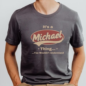 May include: A dark gray t-shirt with a red and beige graphic that says "It's a Michael Thing... You Wouldn't Understand."