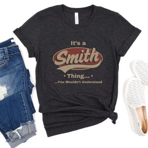 May include: A dark gray t-shirt with a red and white vintage-style logo that says "It's a Smith Thing... You Wouldn't Understand".