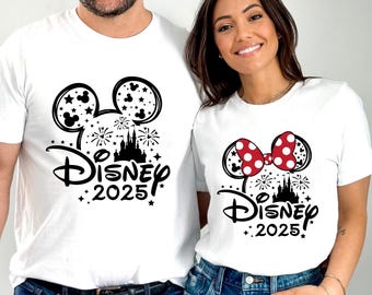 May include: Two white t-shirts with a black and white design featuring Mickey Mouse ears, a castle, fireworks, and the text "Disney 2025". One shirt has a red bow with white polka dots on the ears.