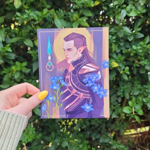 May include: A portrait art print featuring a character with long dark hair and pointed ears, adorned in dark armor and surrounded by blue flowers. A blue and gold weapon is also featured. The artwork has a purple and gold border.