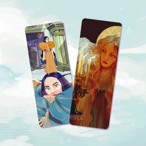 Puede incluir: Dos marcapáginas con ilustraciones. El primer marcapáginas presenta a una mujer con un vestido amarillo y un gran sombrero de plumas de pie en una puerta. El segundo marcapáginas presenta a una mujer con el pelo largo y rubio en un vestido fluido, sosteniendo un candelabro con velas encendidas.