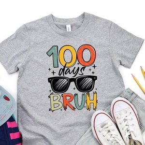 May include: A grey t-shirt with the text "100 days bruh" in colorful letters. The text is surrounded by a rainbow of colors and includes a pair of sunglasses.