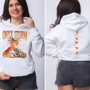 May include: White hoodie with a graphic print of a dragon and the text "ONYX STORM" and "I WILL SAVE HIM". The back of the hoodie has a vertical row of five orange birds.