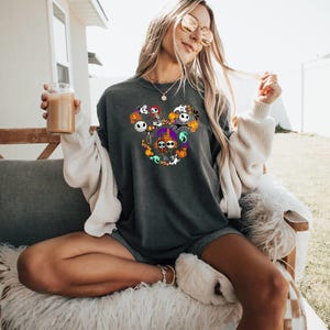 May include: A dark gray long-sleeved t-shirt with a graphic of various characters from the Nightmare Before Christmas movie in a Mickey Mouse shape. The characters are in various colors, including black, white, green, orange, and purple.