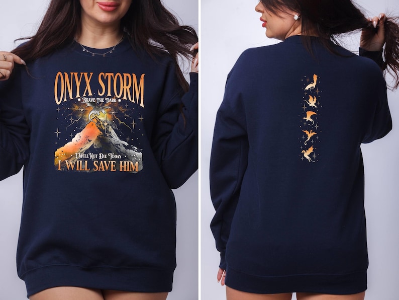 May include: Navy blue sweatshirt with a graphic print of a mountain range and the text "ONYX STORM - BRAVE THE DARK - I WILL NOT DIE TODAY I WILL SAVE HIM". The back of the sweatshirt features a vertical row of five orange dragon silhouettes.