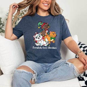 May include: A navy blue t-shirt with a graphic of three cats wearing Christmas lights. The text "Everybody Loves Christmas" is printed below the graphic.