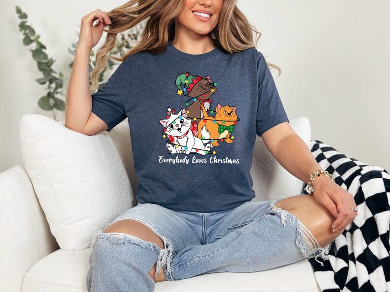 May include: A navy blue t-shirt with a graphic of three cats wearing Christmas lights. The text "Everybody Loves Christmas" is printed below the graphic.