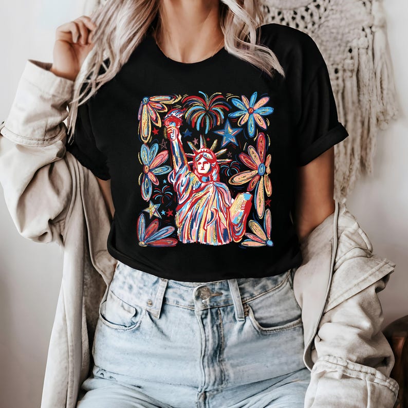 May include: A black t-shirt with a colorful graphic of the Statue of Liberty surrounded by fireworks and flowers. The graphic is in a square frame.