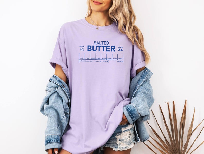 May include: A lilac t-shirt featuring the words "Salted Butter" in blue, with a graphic showing measurement conversions. The shirt is made of a soft, comfortable material.