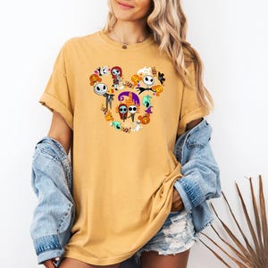 May include: A yellow t-shirt with a Mickey Mouse silhouette made up of characters from the Nightmare Before Christmas. The characters include Jack Skellington, Sally, Oogie Boogie, and Zero.