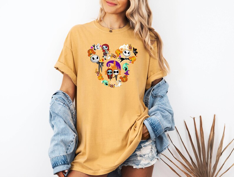 May include: A yellow t-shirt with a Mickey Mouse silhouette made up of characters from the Nightmare Before Christmas. The characters include Jack Skellington, Sally, Oogie Boogie, and Zero.