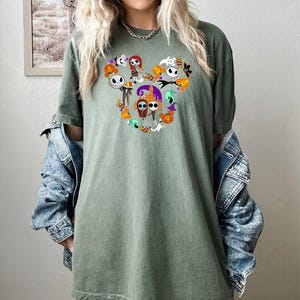 May include: A green t-shirt with a Mickey Mouse silhouette made up of characters from the Nightmare Before Christmas. The characters include Jack Skellington, Sally, Oogie Boogie, and Zero.