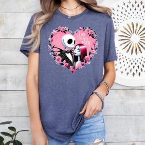 May include: A navy blue t-shirt with a pink heart graphic featuring Jack Skellington and Sally from The Nightmare Before Christmas. The text inside the heart reads "Love You To Death."