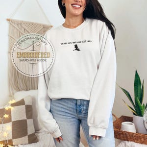May include: White sweatshirt with the text "We do not eat our allies." and a black silhouette of a bat. The sweatshirt is embroidered with the text "Personalized Gift Embroidered Sweatshirt & Hoodie".