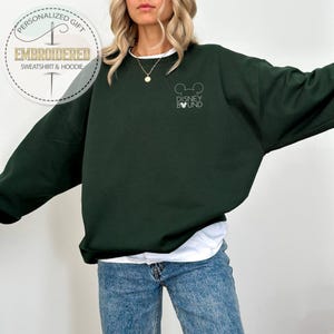 May include: A dark green sweatshirt with the text "Disney Bound" and a Mickey Mouse head design. The sweatshirt also has a circular logo that says "Personalized Gift" and "Embroidered Sweatshirt & Hoodie".