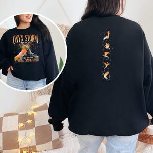 May include: Black sweatshirt with a graphic of a dragon on the front and a row of dragons on the back. The text on the front reads "Onyx Storm - Rise to the Stars - I Will Save Him".