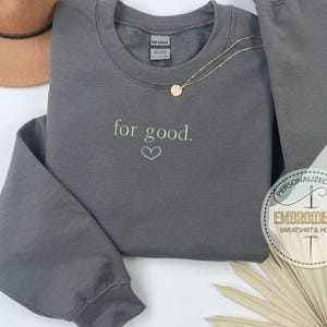 May include: Gray sweatshirt with the text "for good." embroidered in green on the front. The sweatshirt has a crew neck and long sleeves.