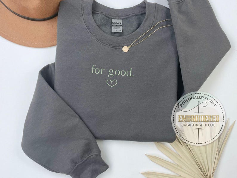 May include: Gray sweatshirt with the text "for good." embroidered in green on the front. The sweatshirt has a crew neck and long sleeves.