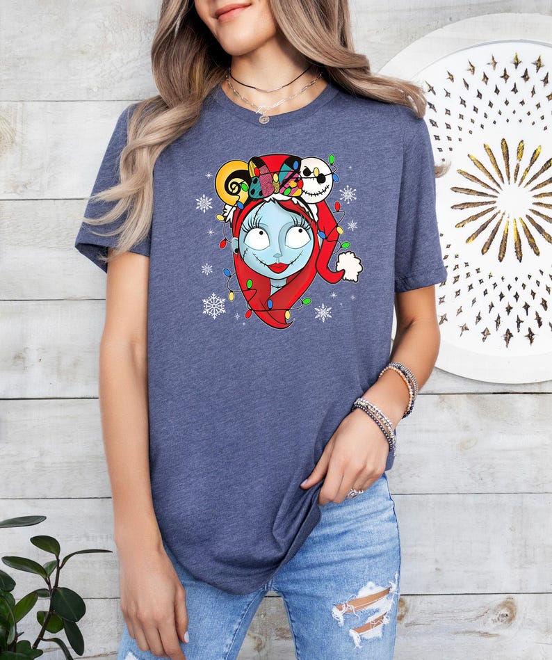 Pu&ograve; includere: Una maglietta blu con una grafica di un personaggio di The Nightmare Before Christmas che indossa un cappello da Babbo Natale e circondato da luci di Natale e fiocchi di neve.