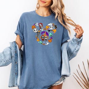 May include: A blue t-shirt with a graphic of various characters from the Nightmare Before Christmas movie, arranged in the shape of Mickey Mouse ears.