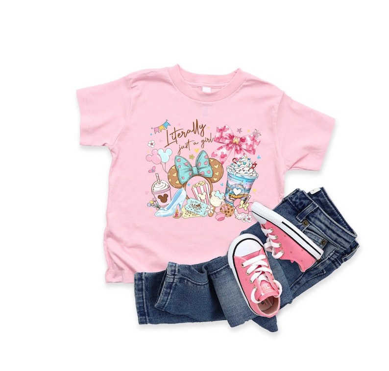 May include: A pink t-shirt with the text "Literally just a girl" and a graphic of a Minnie Mouse bow, desserts, and shoes. Paired with blue denim jeans and pink sneakers.