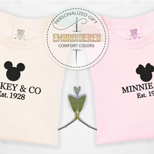 May include: Two t-shirts, one cream and one pink, with black Mickey and Minnie Mouse head designs. The cream shirt says "Mickey & CO Est. 1928" and the pink shirt says "Minnie & CO Est. 1928". A circular graphic reads "Personalized Gift Embroidered Comfort Colors".