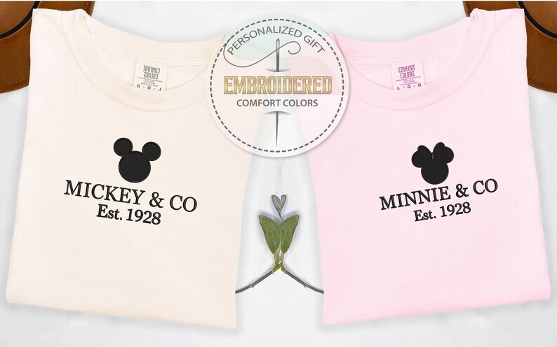 May include: Two t-shirts, one cream and one pink, with black Mickey and Minnie Mouse head designs. The cream shirt says "Mickey & CO Est. 1928" and the pink shirt says "Minnie & CO Est. 1928". A circular graphic reads "Personalized Gift Embroidered Comfort Colors".
