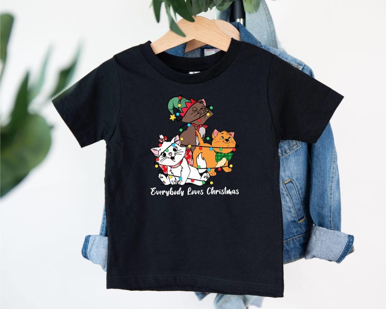 May include: Black t-shirt with a graphic of three cats dressed as Christmas characters. The text "Everybody Loves Christmas" is printed below the graphic.