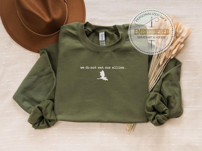May include: A green long-sleeved sweatshirt with the text "we do not eat our allies." and a white dragon silhouette embroidered on the front.